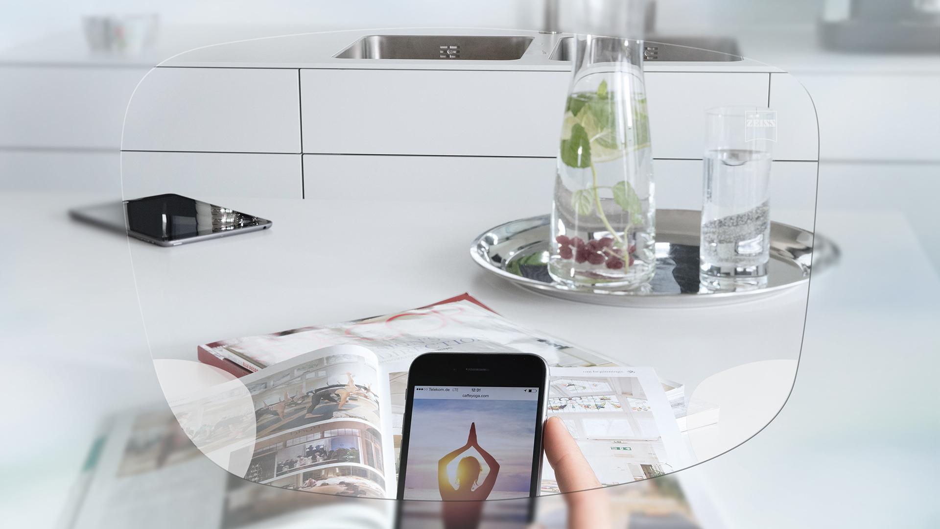 Pohľad cez jednoohniskové okuliarové šošovky ZEISS EnergizeMe na obrazovku smartfónu a usporiadaný kuchynský stôl
