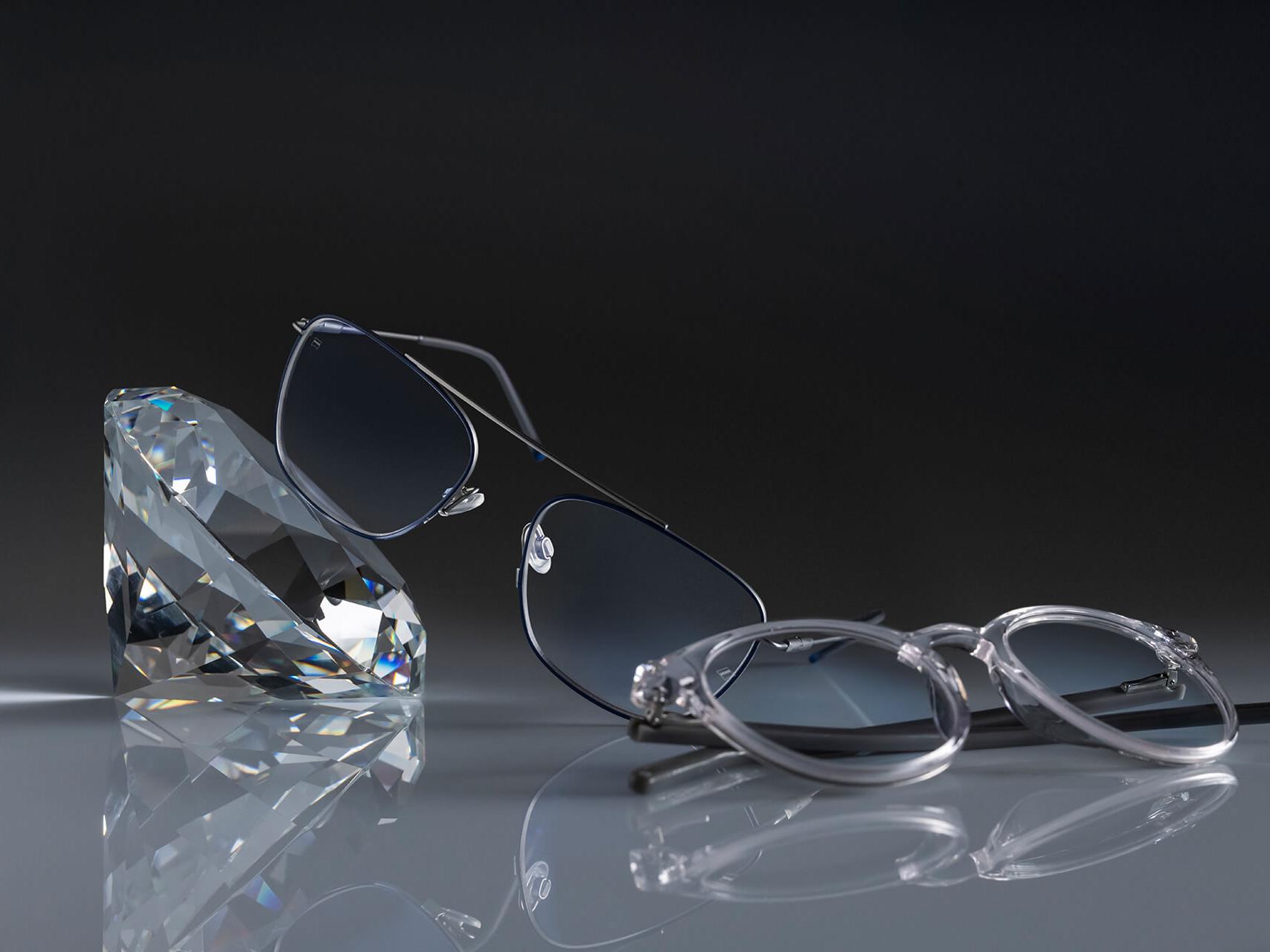 Dva páry okuliarov so šošovkami ZEISS, ktoré majú vôbec najtvrdší povrch ZEISS – DuraVision® Platinum. Jeden pár okuliarov je opretý o kryštál, ten druhý je položený rovno na podklade. Oba majú číre šošovky bez žiadnych modrastých odrazov.