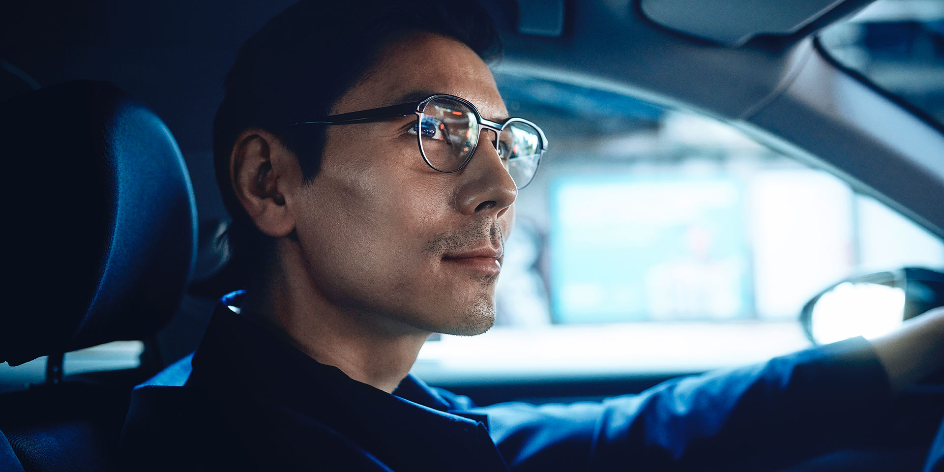 Muž šoférujúci auto, vyzerajúci sebavedome s miernym úsmevom na ceste. Má šošovky single vision ZEISS DriveSafe.