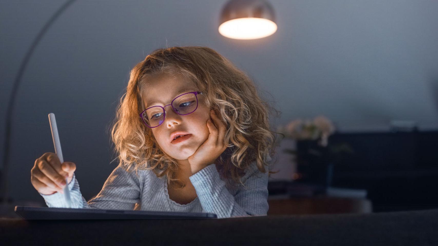 Malé dievča v tmavej obývacej izbe sa pozerá na tablet.