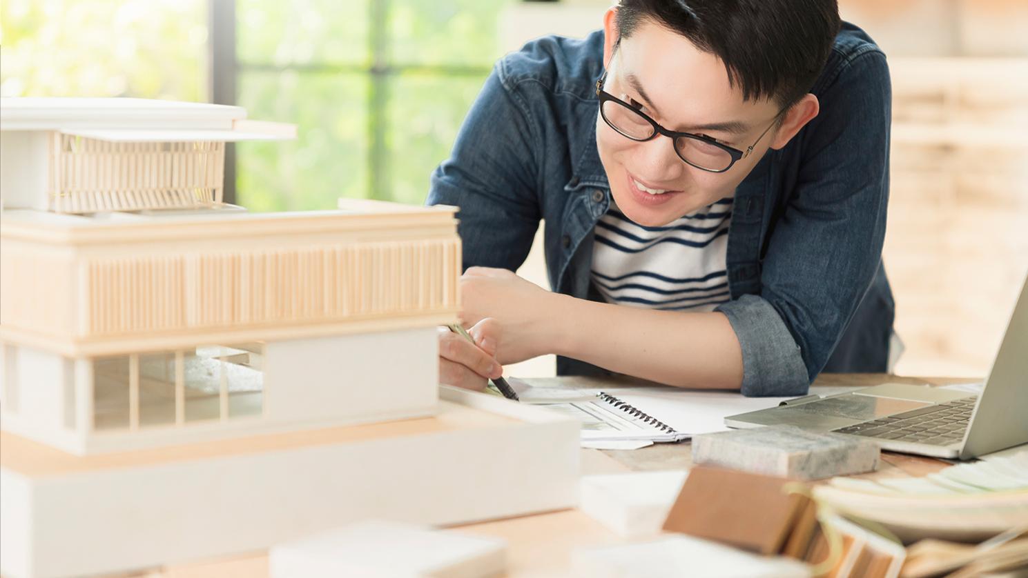 Muž v strednom veku s krátkymi čiernymi vlasmi v okuliaroch ZEISS Office, ktoré mu pomáhajú zaostrovať na detaily zložitého architektonického modelu. 