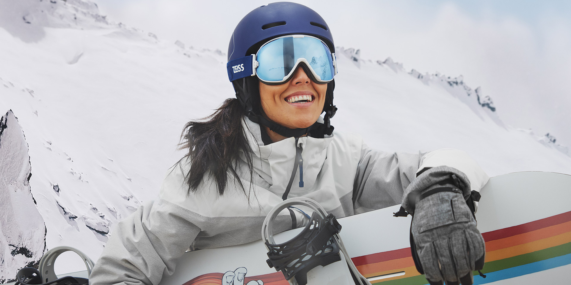 Mladá žena v lyžiarskych okuliaroch s technológiou ZEISS Interchangeable a držiaca snowboard.
