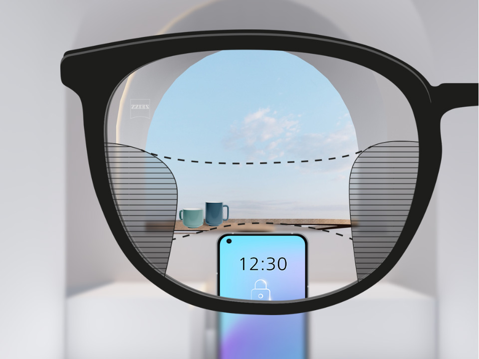 Obrázok zorného uhla so šošovkami ZEISS Progressive SmartLife so smartfónom a šálkami v pozadí, zatiaľ čo šošovka je úplne jasná s tenkými rozmazanými políčkami vľavo a vpravo.
