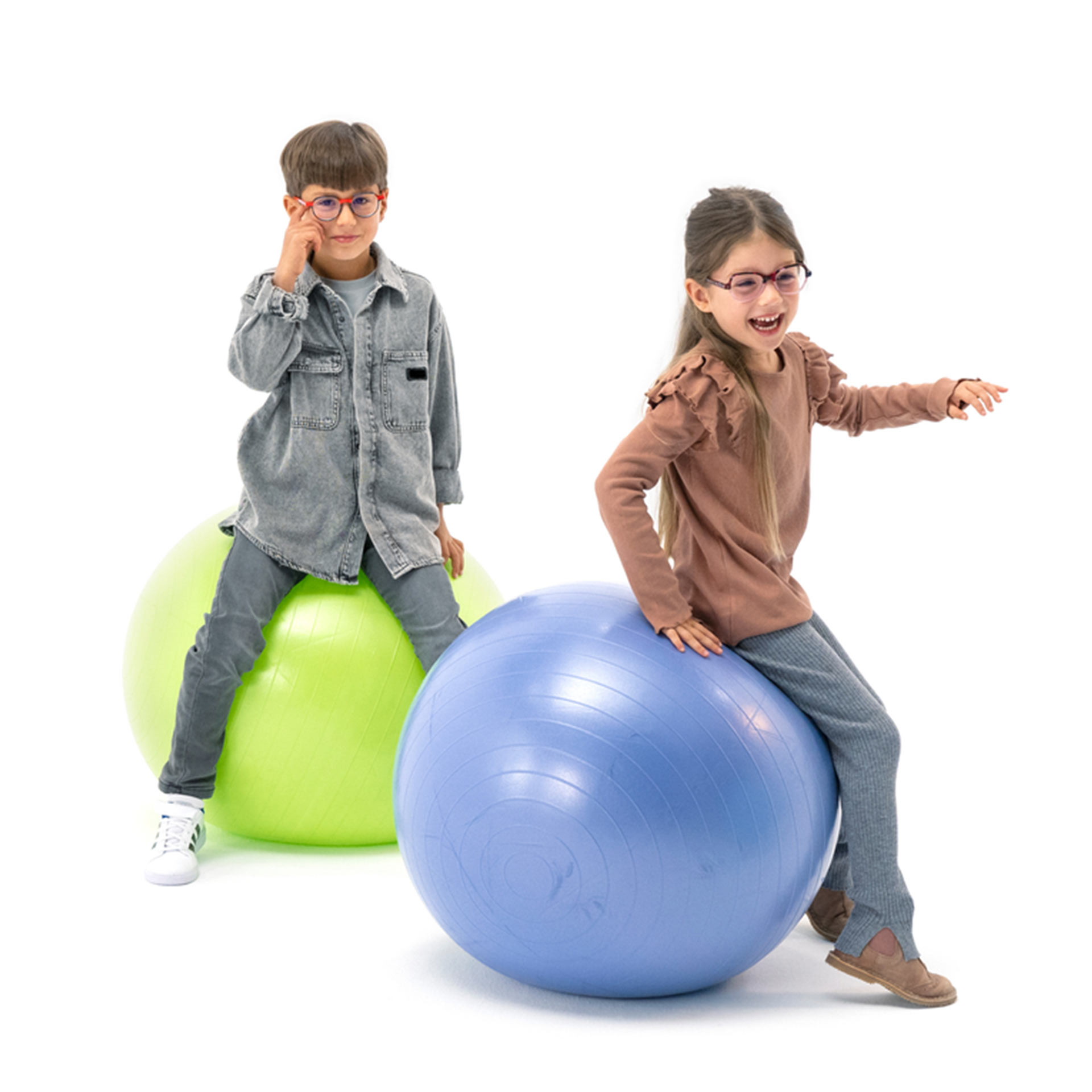 Chlapec a dievča, obaja nosiaci okuliare, sa hravo odrážajú na gymnastických loptách.
